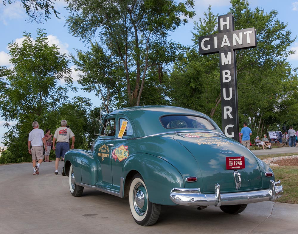 vintage car parked in front of replica sign for red's giant hamburg